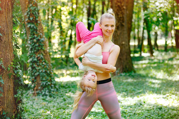 Happy woman holding little girl. Mother and daughter exercise in park and having fun