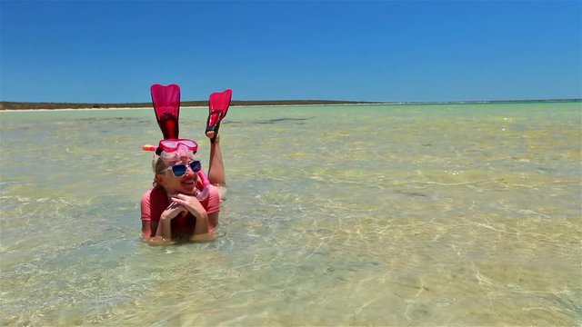Caucasian young woman with snorkeling wetsuit, mask and fins in pink and peach color, sunbathing in the tropical natural pool of Little Lagoon in Shark Bay, Denham, Western Australia. Copy space.