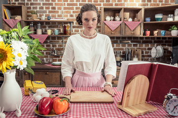 Fototapeta premium serious adult housewife in vintage clothes looking at camera at kitchen