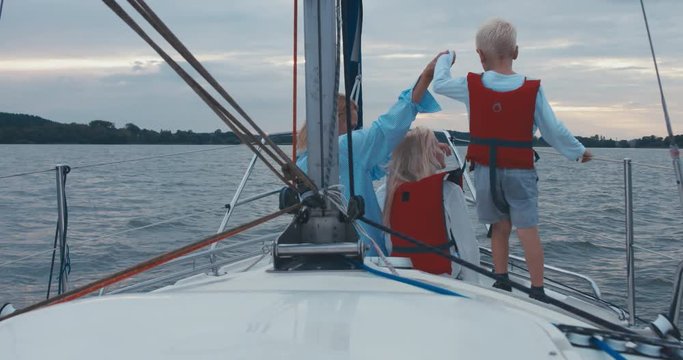 Young adult mid-30s Caucasian female and her kids, daughter and son sailing on yacht, sunset in the background. 4K UHD 60 FPS SLO MO