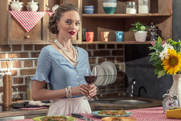 beautiful adult housewife with glass of red wine at kitchen