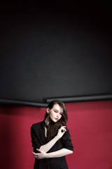 Portrait of a beautiful model girl in a business suit on a ragged red and black background. Hands touching her lips and hair.