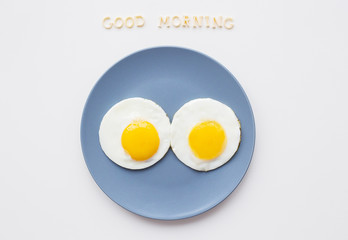 two eggs on a plate and a yellow napkin, inscription Good Morning