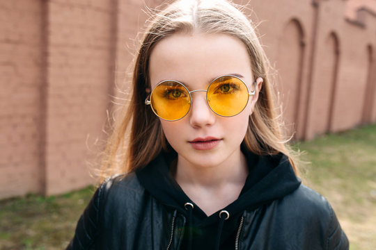 beautiful fashionable kid girl in yellow sunglasses in city street