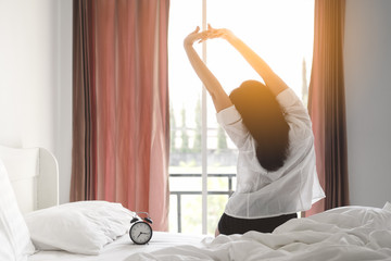 Happy asian woman stretching on bed after waking up at morning in bedroom.