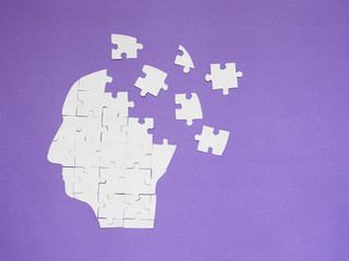 White jigsaw puzzle as a human brain on purple background w/ copy space. Creative idea for memory...