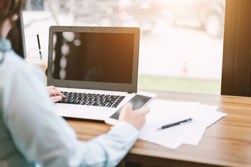 Fototapeta premium Close-up of business female working with Mockup image of laptop with blank black screen make a note in coffee shop like the background.