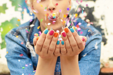 Fashionable girl with bright colorful nail designs blows confetti in her hands.Nails art.Color manicure. - obrazy, fototapety, plakaty