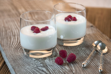 Yogurt with raspberry on wooden gray table.