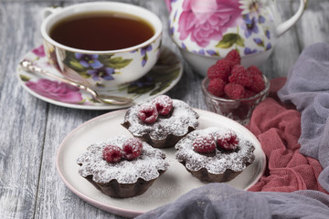 Cake with raspberries and sugar powder on the table with tea teapot.