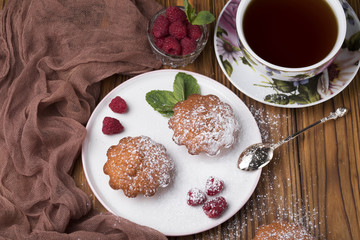 Muffin with raspberries and sugar powder on the table with tea teapot.