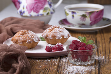 Capcake with raspberries and sugar powder on the table with tea teapot.