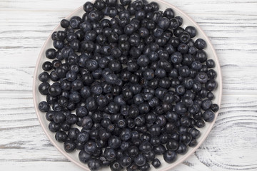 Fresh blueberry in ceramic bowl on wooden table.