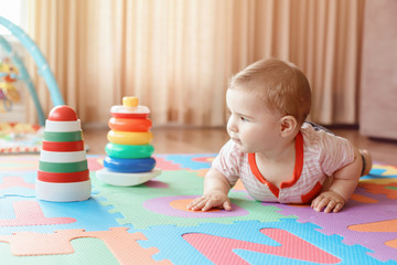 Portrait of cute adorable blond Caucasian smiling child boy with blue eyes crawling on floor in kids children room. Little baby playing with toys on playmat at home. Early education development