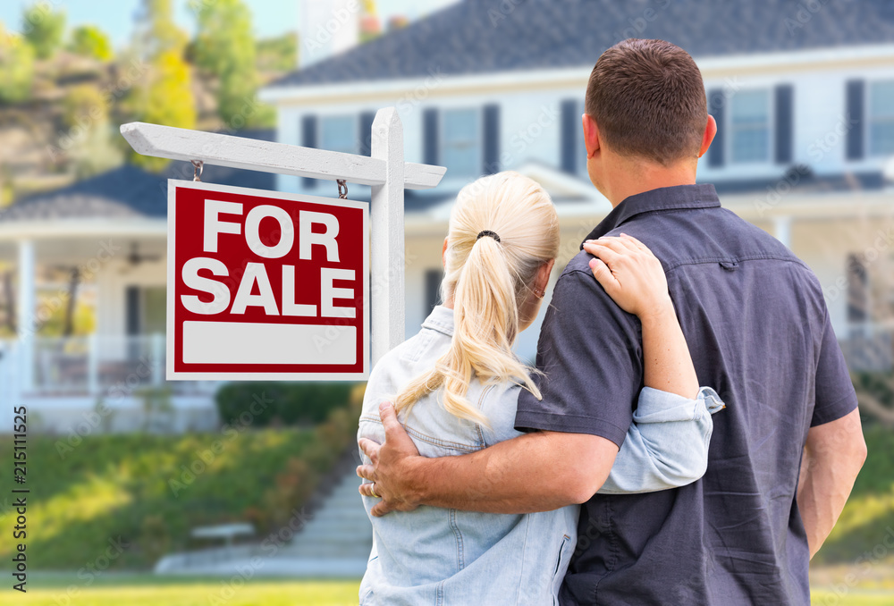 Wall mural young adult couple facing front of for sale real estate sign and house