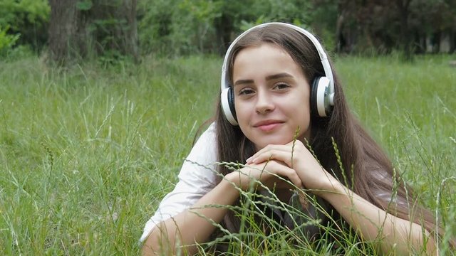 A girl in the nature listens to music. Beautiful girl in headphones lies on green grass.