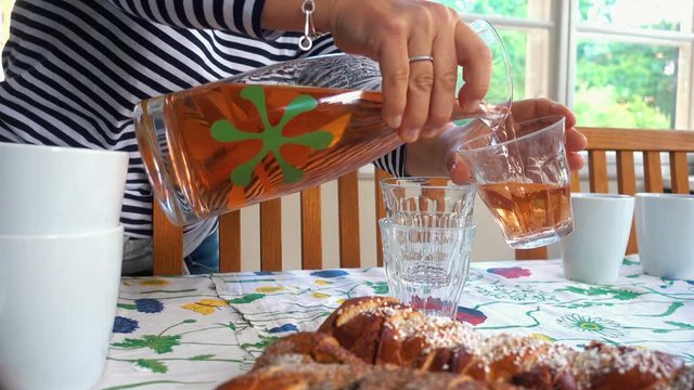 women is pouring juice with cinnabonn buns in the foreground preparing for swedish midsummerfika