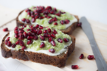 Pieces of toasted bread with cottage cheese, avocado and pomegranate kernels