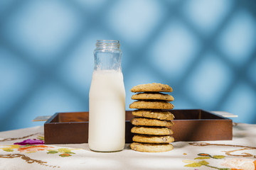 Cookie pile and milk bottle in a table. Morning sun in a blue background with texture.
