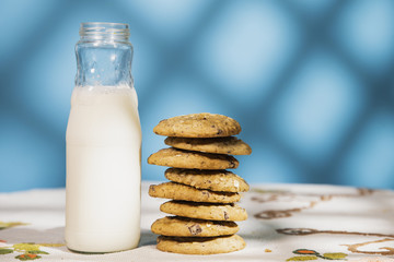 Cookie pile and milk bottle in a table. Morning sun in a blue background with texture.