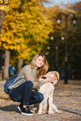 Beautiful young blonde is walking in the park with her labrador in the park in the fall. The woman crouched beside her retriever.