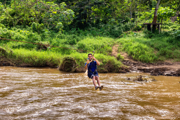 Young man goes through a river on zip line in Chiang Mai in Thailand