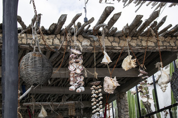 Closeup of rustic stick roof in Mexico with shells and woven baskets hanging from ends of sticks by old ropes and rusty chains with cacti outside