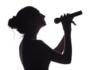 silhouette of beautiful girl singing into microphone, profile of young woman face performing lyric...