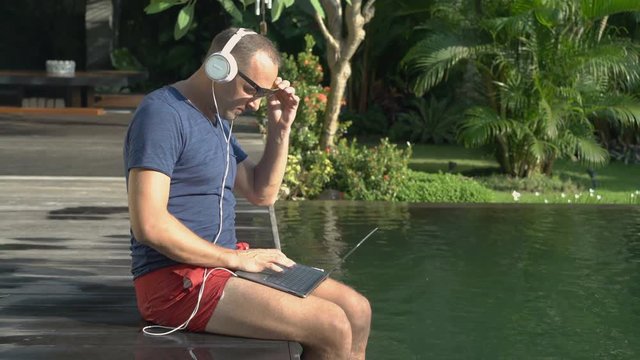 Young man watching movie on laptop computer by the swimming pool
