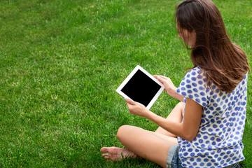 young girl blogger. the girl is working on the tablet. the girl is sitting on the green lawn