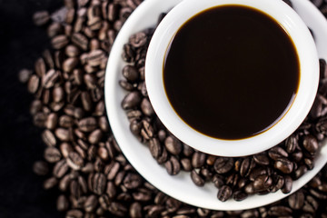 Dark coffee in white plate with coffee beans on black background.
