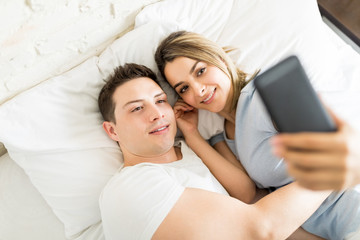 Romantic Couple Taking Selfie On Phone While Lying On Bed