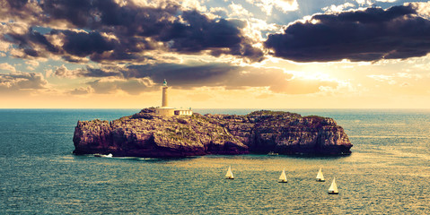 Paisaje marino de faro sobre las rocas en el mar. Barcos y puesta de sol. Isla de Mouro en Santander, Cantabria. © C.Castilla