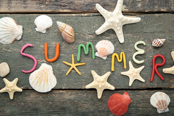 Inscription Summer by plasticine with seashells on grey wooden table
