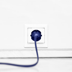 Electric white socket and one plugged in power cord on white wall background
