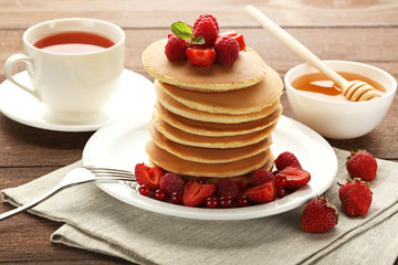 Tasty pancakes with berries and cup of tea on wooden table