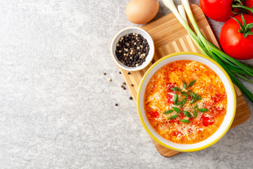 Traditional chinese egg drop soup with tomato and green onion in bowl on gray stone background