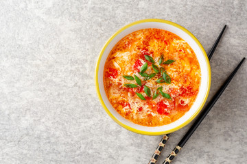 Traditional chinese egg drop soup with tomato and green onion in bowl on gray stone background