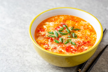 Traditional chinese egg drop soup with tomato and green onion in bowl on gray stone background