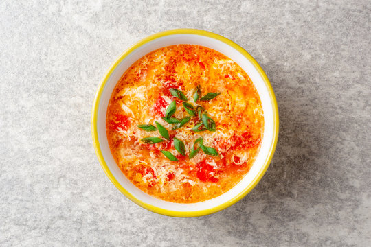 Traditional chinese egg drop soup with tomato and green onion in bowl on gray stone background