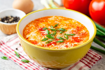 Traditional chinese egg drop soup with tomato and green onion in bowl on gray stone background