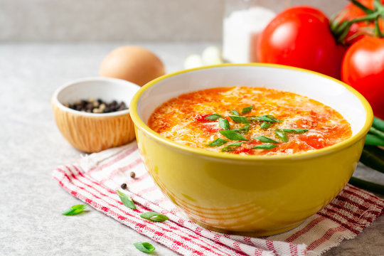 Traditional chinese egg drop soup with tomato and green onion in bowl on gray stone background