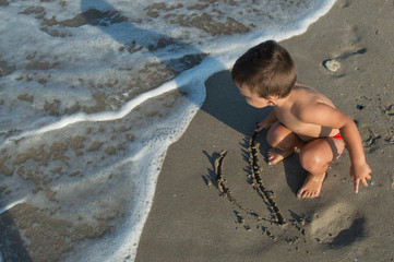 the boy draws on the sand, and the wave is washing his drawing