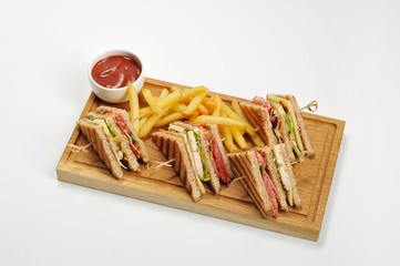 Club-sandwich and french fries on a light wooden board. Next to the potatoes is a cup of ketchup. White background. Close-up. 