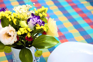On the table are empty plates and a bouquet of flowers in a decorative vase. Colorful tablecloth on the table. Rustic background. The concept of a holiday. Selective focus, copy space.