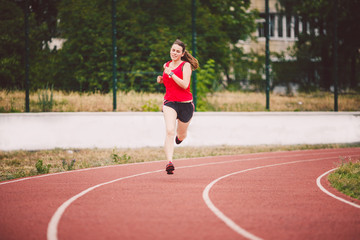 Beautiful young athlete Caucasian woman with big breasts in red T-shirt and short shorts jogging,...