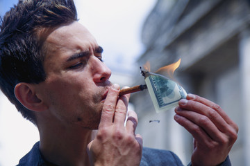 Young brutal businessman lighting cigar with $100 dollar bill