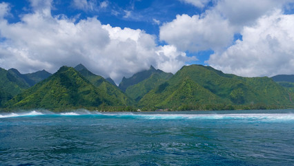 Fototapeta na wymiar Beautiful ocean waves approach the vivid green mountains of the lush island.