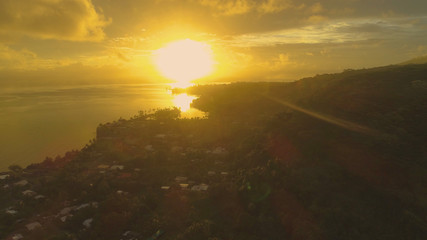AERIAL: Blinding golden sunbeams shine on the coastline of tropical island.