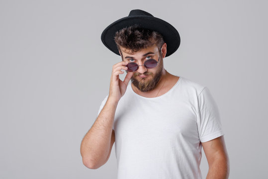 A young successful man with a beard in sunglasses and a hat on a gray background with space for text.